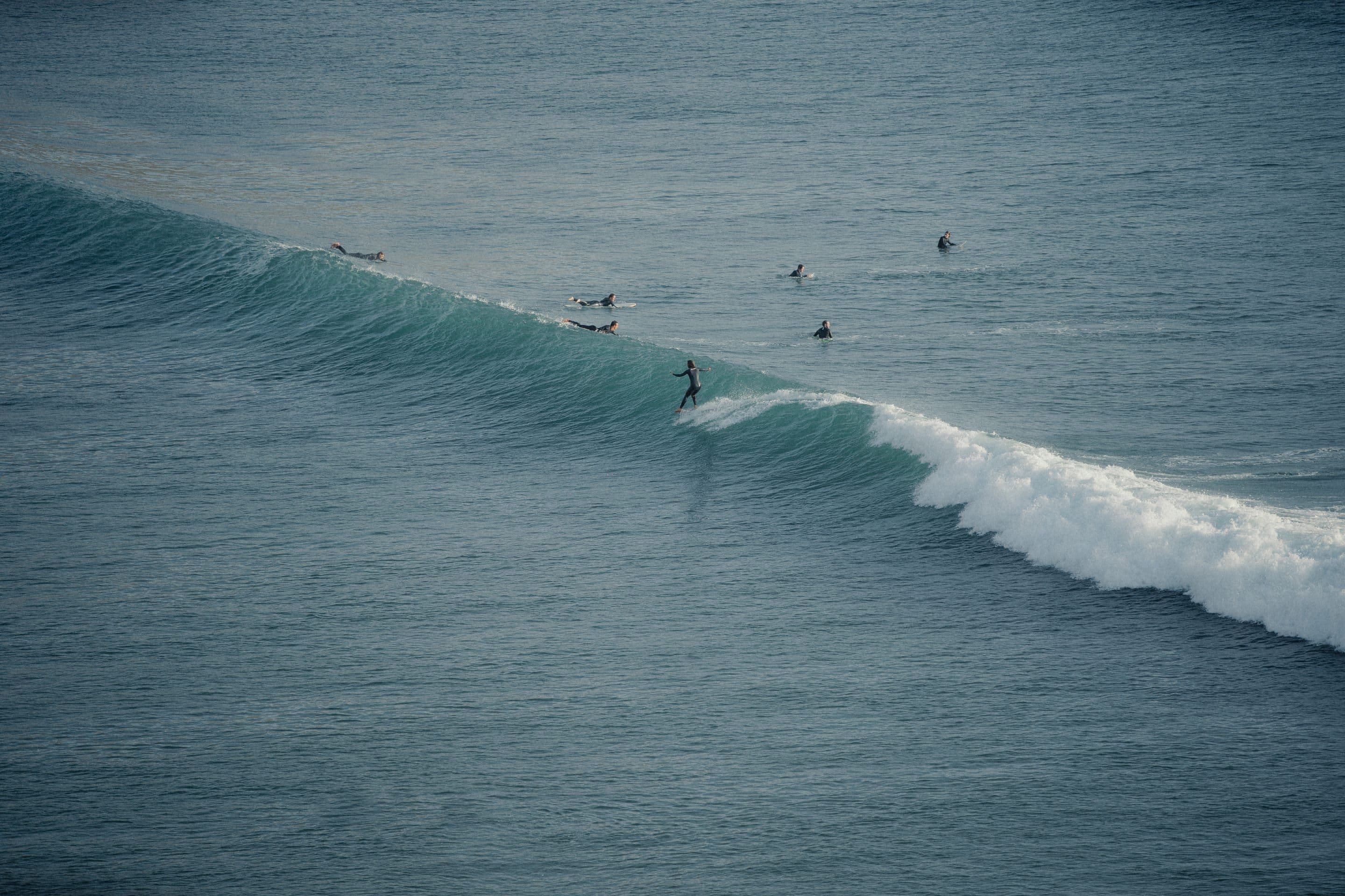 A surfer trimming down the face of a clean right-hander at Imsouane while the rest of the group waits in the lineup.